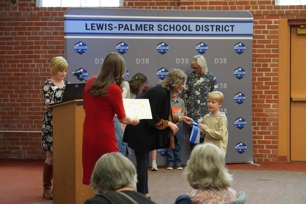 Boy receives a ribbon and cash award at art awards ceremony.
