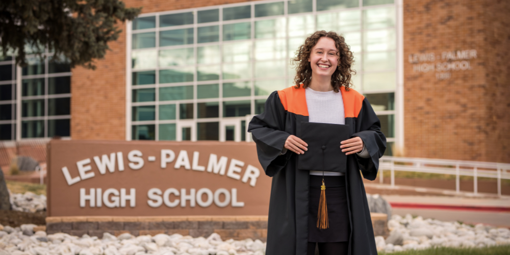 Lilly Font standing in front of the lewis-palmer high school sign in a graduation gown