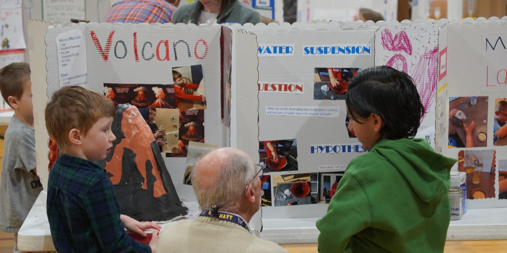 Two students discuss their science fair projects with a judge at Bear Creek's Science Fair and STEAM Day