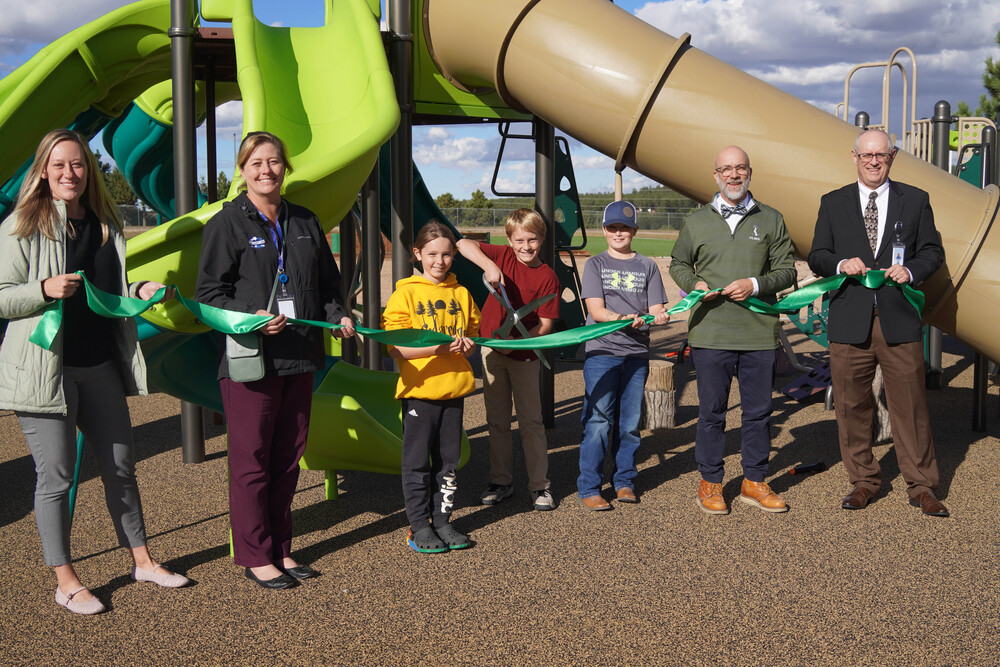 Kids and adults stand in front of playground cutting a ribbon.
