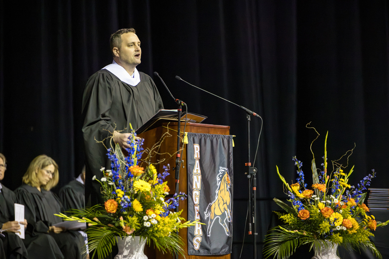 Man speaks at podium in graduation gown.