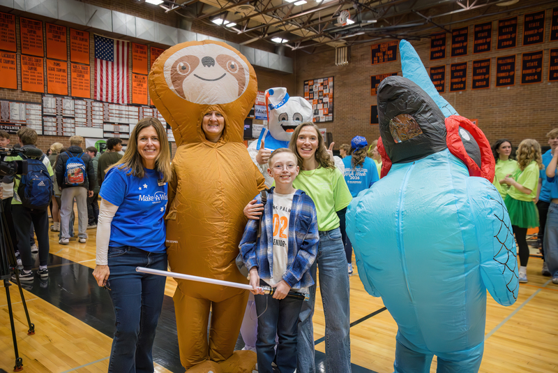 Wish Kids Alex posing with his mom, a light saber, a make-a-wish representative, and two people in blow up costumes