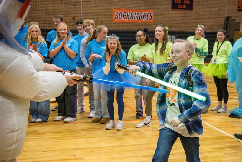 Wish Kid Alex having a light saber fight with someone in a costume while they are being cheered on by the LPHS Student Council