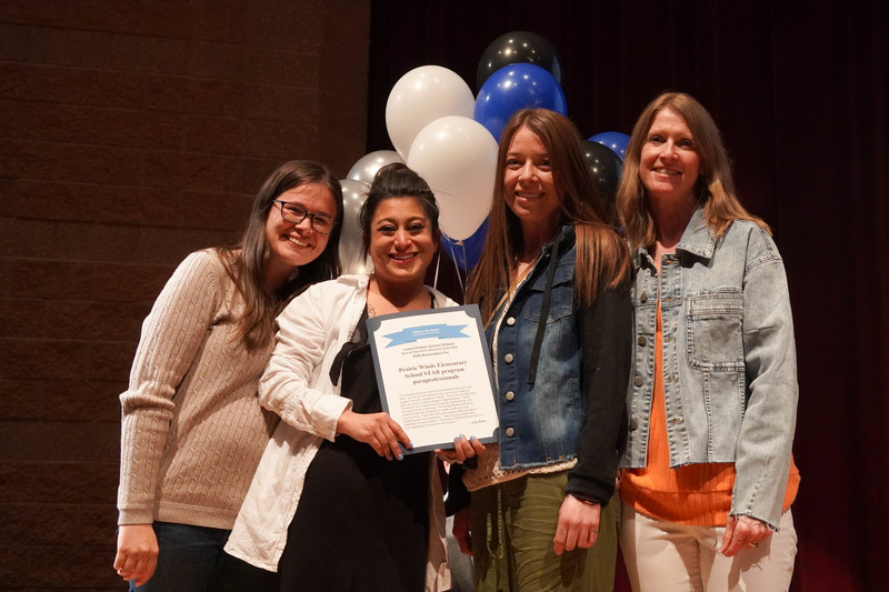 Four female staff members in front of balloons with a certificate.