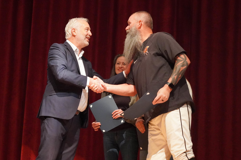 Man presents a certificate to a bearded staff member.
