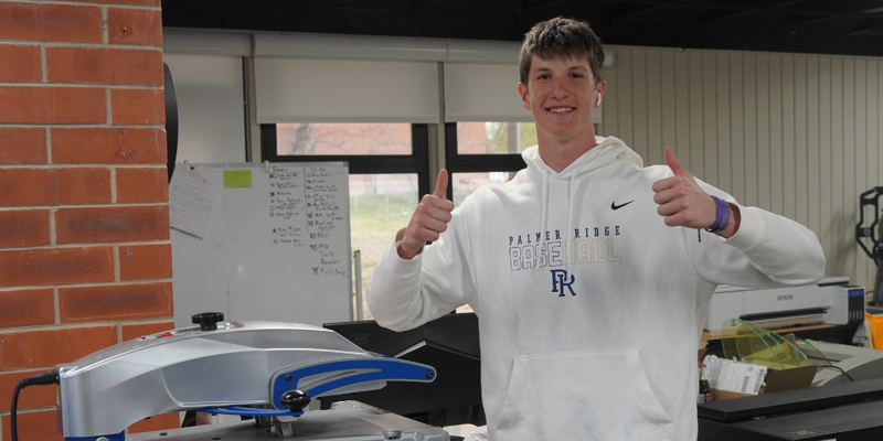 A male student giving a thumbs up while working at The Enterprise