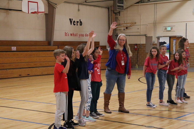 Groups of students lined up in school auditorium with one group raising their hands in the air