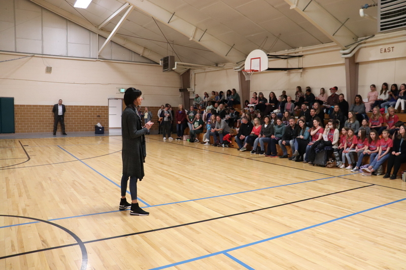 School staff member speaking to attendees seated in bleachers of school auditorium