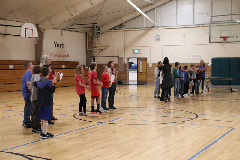 Groups of students lined up in school auditorium with a school staff member standing next to each group of children