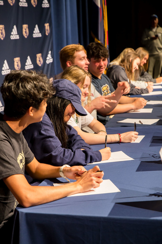 Group of palmer ridge high school students seated behind tables on stage with papers and pens in hand