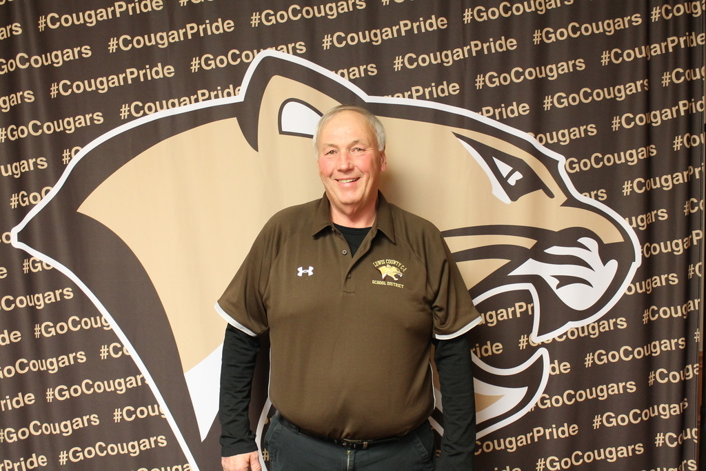 Robert Reed Miller, president of the Lewis County C-1 Board of Education, smiles while standing in front of a cougar-themed “Cougar Pride” backdrop, recognized for his 34 years of dedicated service to the district.