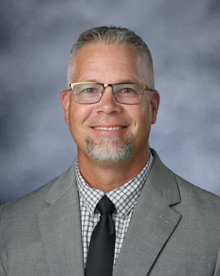 A photo of Mr. Scifres in a gray suit jacket, white shirt, and black tie.
