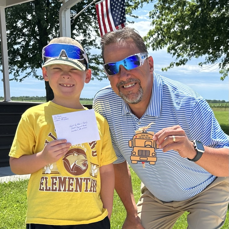 Photo of Wyatt VanMeter with Mr. French in a yard with an American flag in the background with Wyatt holding a Thank You card and Mr. French holding a custom made card holder in the shape of a bus.
