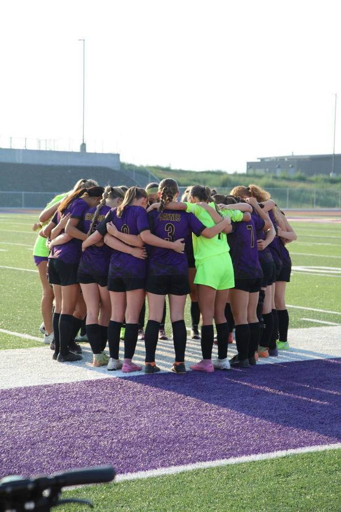 Lewiston Bengal soccer girls team in purple jerseys with their arms around each other in a huddle