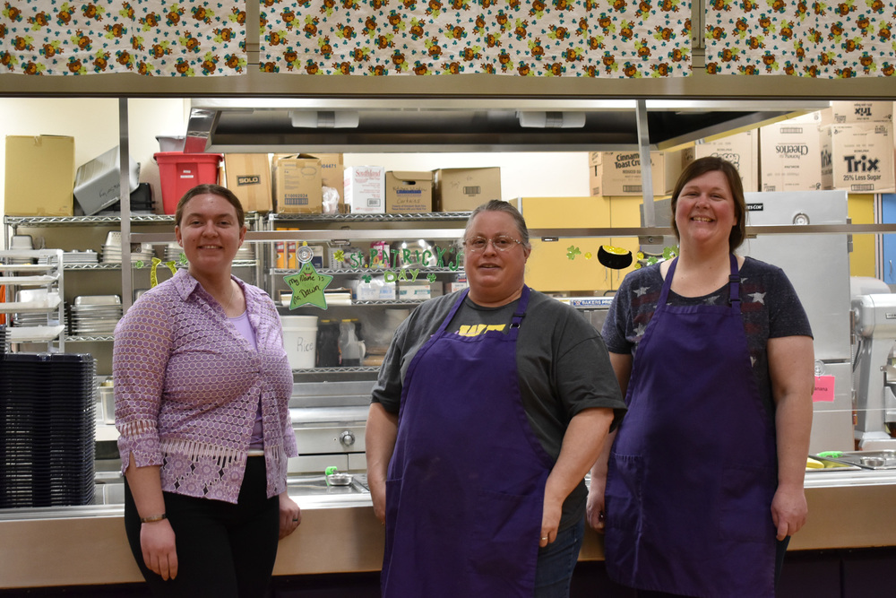 Three women stand in front of the lunchroom window