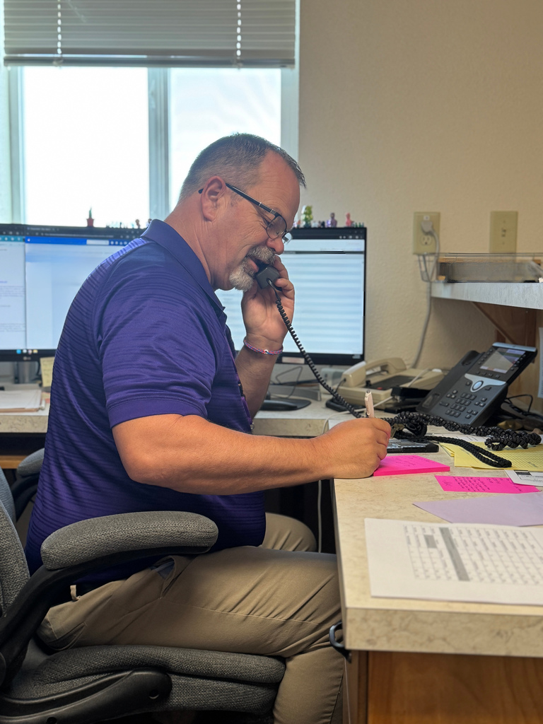 Tim Sperber in a purple shirt and glasses answering a phone