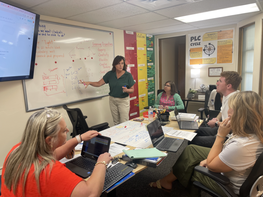 woman with dark hair, a green shirt on, and khaki pants instructing math