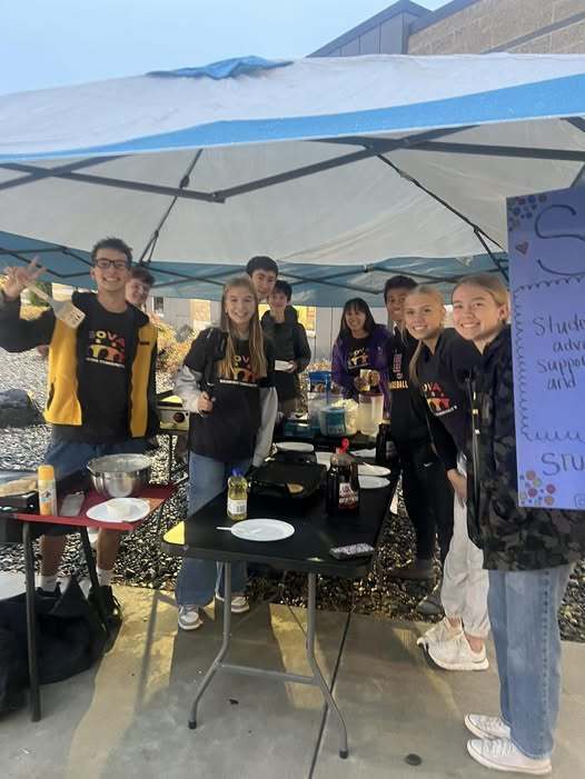 students making pancakes standing under a tent