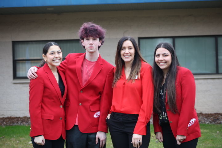 3 students and advisor standing together in red blazers