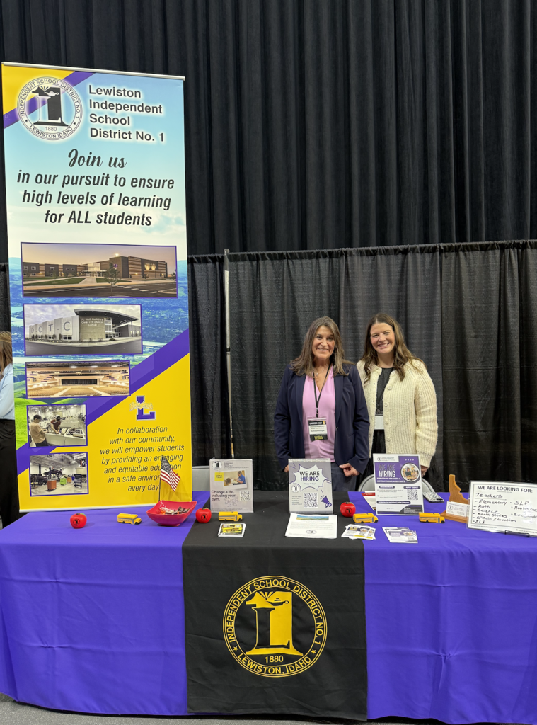 two women standing behind a purple table with a banner of the district beside them