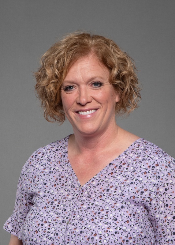 Deedra Hastings has curly blond hair and is wearing a purple floral top