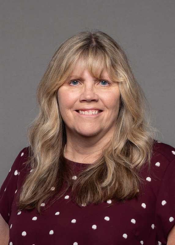 woman with blonde curly hair and a maroon shirt with white polka dots