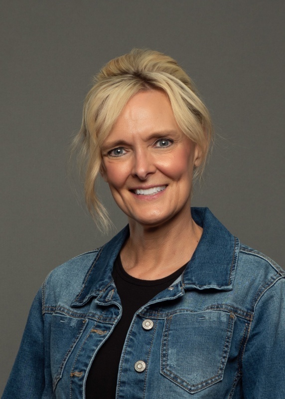 Kristi Murphy has blonde hair, a black shirt, and denim jacket