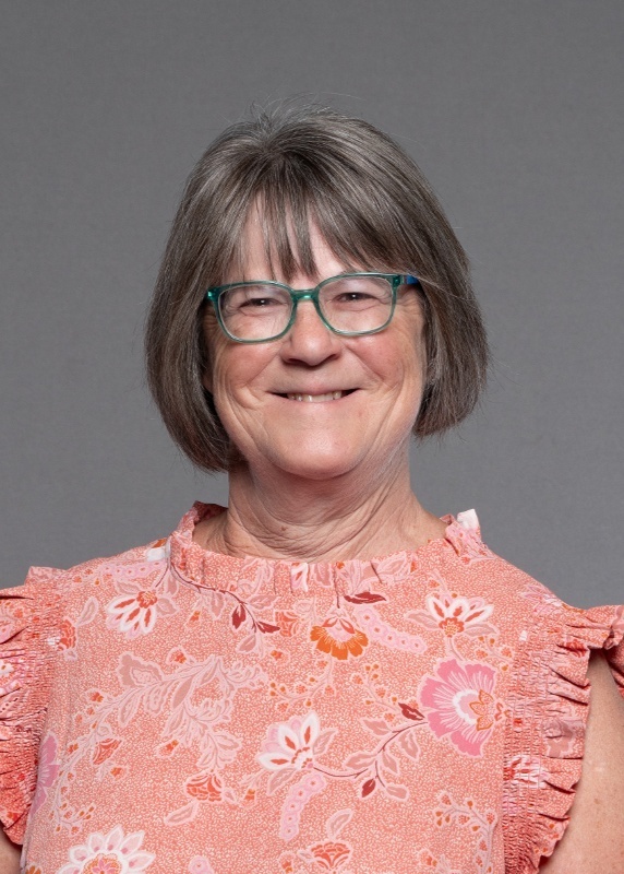 Rebecca Sater has short grey hair, glasses, and is wearing a peach colored top