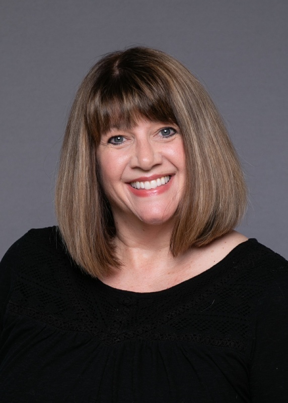 woman with shoulder length brown hair and bangs and a black top on