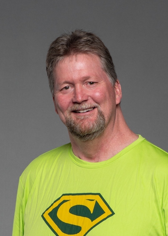 man in a bright green shirt with a superman S on it, brown hair, and facial hair