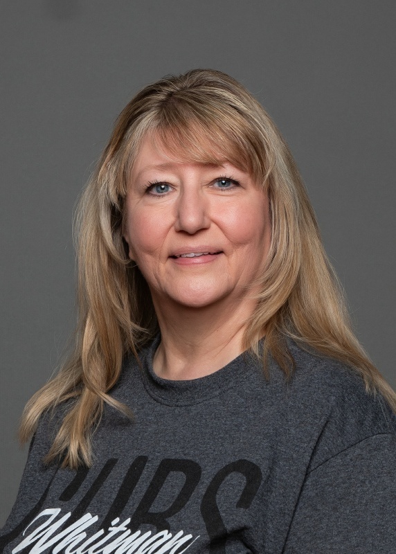 woman with blonde hair and bangs, wearing a grey shirt