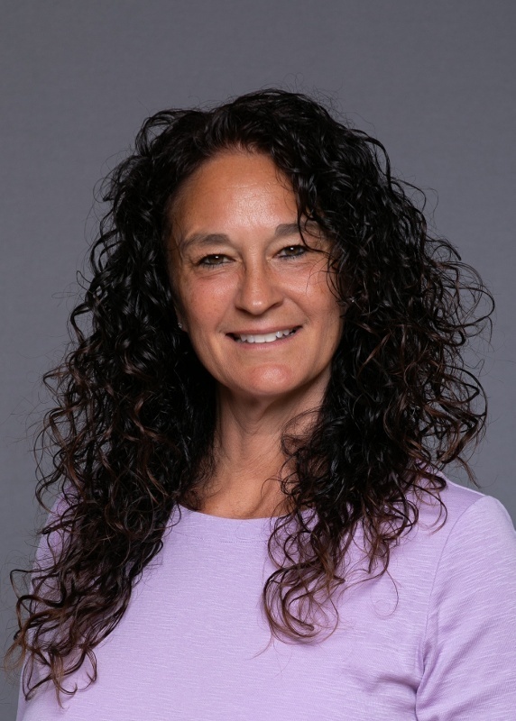 woman with dark curly long hair and wearing a purple shirt