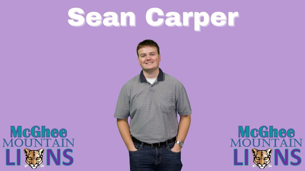 Sean has short brown hair and is wearing a grey polo and jeans