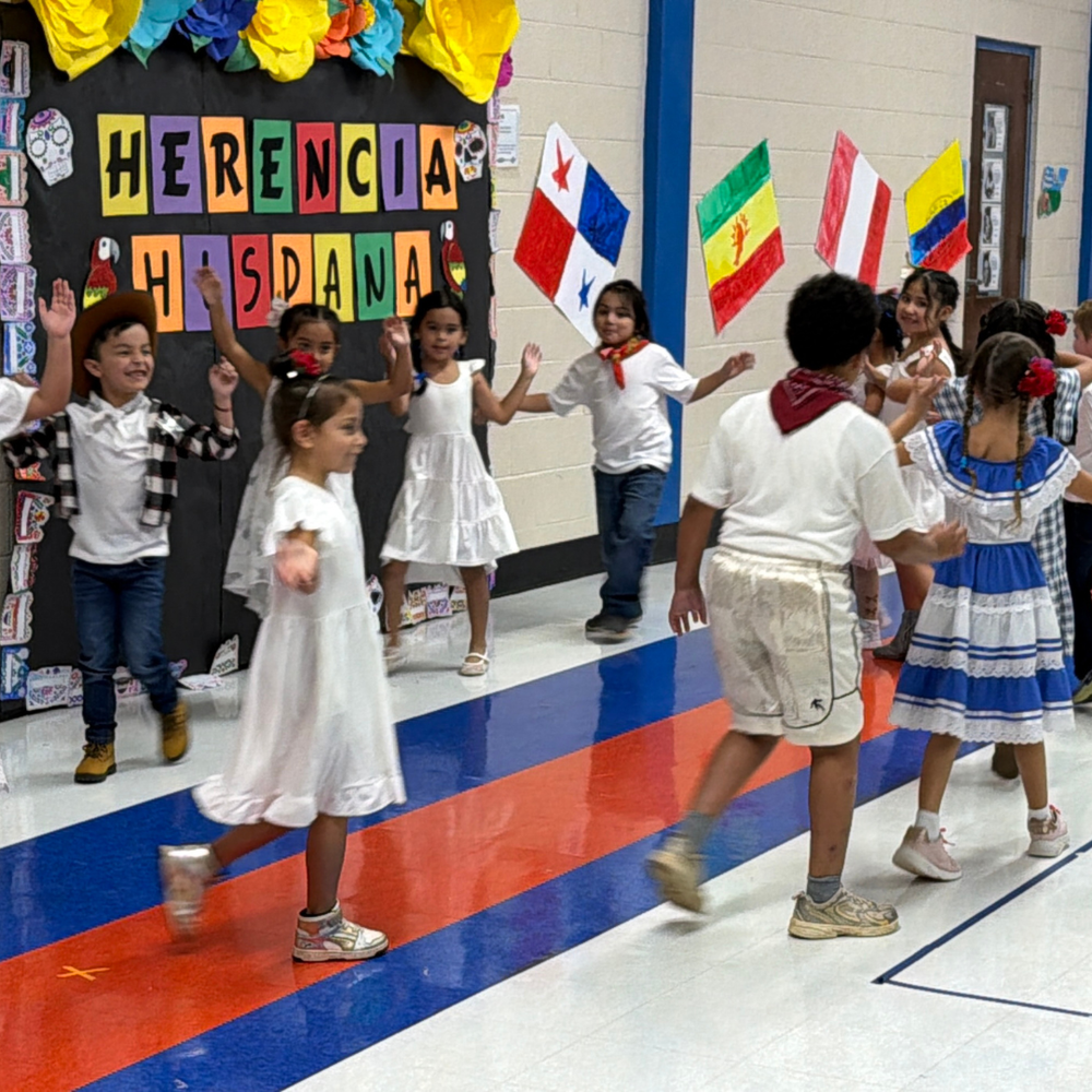 Pickett Elementary School students dance in front of a colorful Hispanic Heritage Month display featuring flags and cultural decorations.
