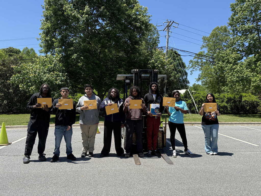 A group of students proudly pose together while holding certificates after becoming newly certified forklift operators through a Career and Technical Education program at Lexington City Schools. The students are standing indoors and smiling to celebrate earning an industry-recognized workforce credential.