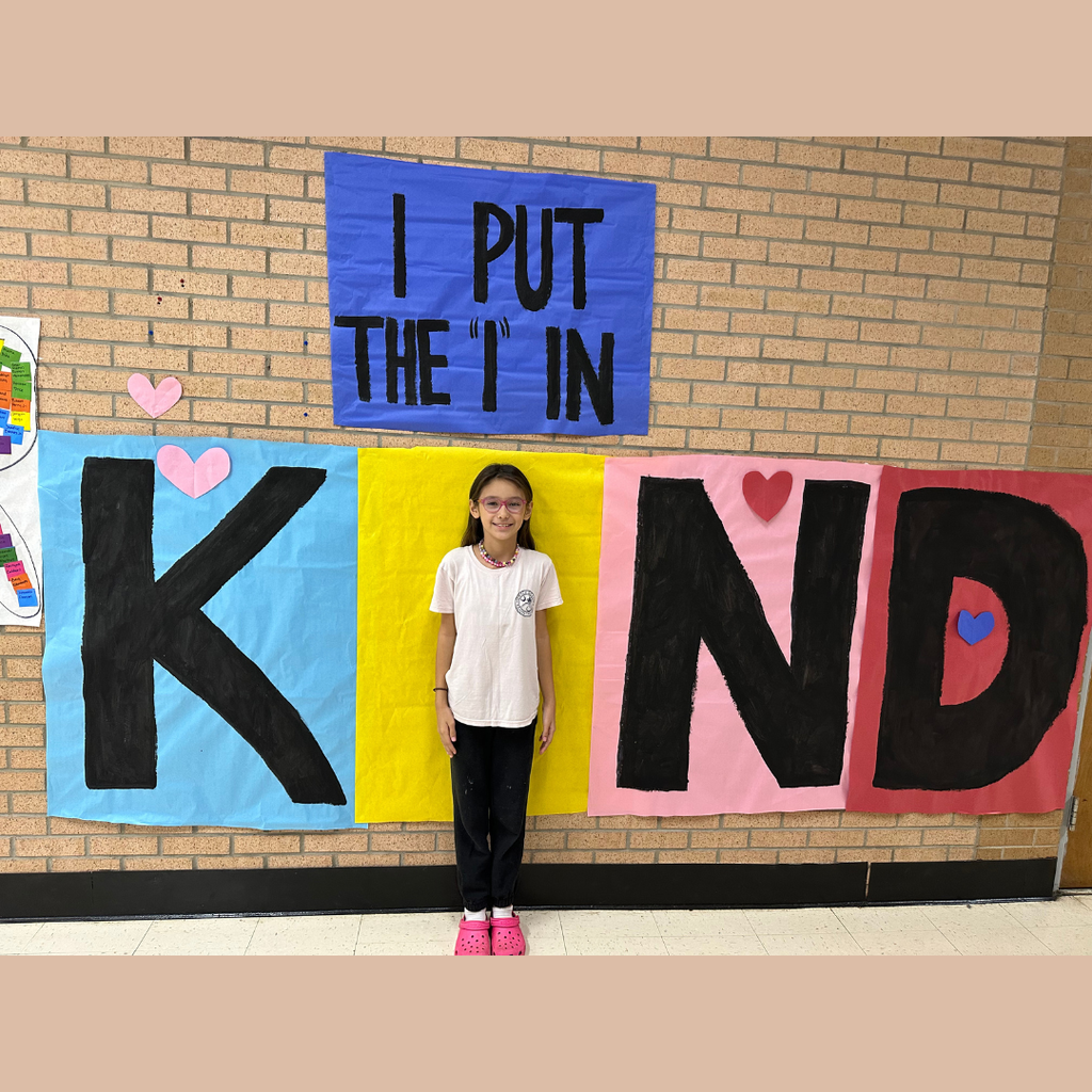 A student at Southwest Elementary Global Academy stands in front of a colorful “I Put the I in Kind” display decorated with hearts to promote kindness and inclusion.