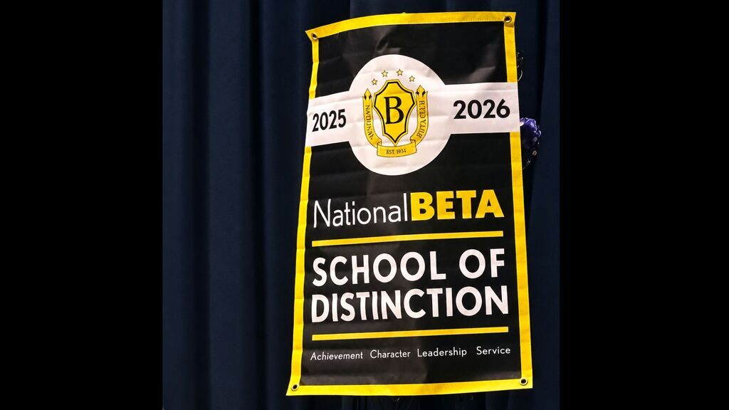 A black and gold National Beta School of Distinction banner hangs against a dark curtain, recognizing Lexington Senior High School for the 2025–2026 school year. The banner features the National Beta emblem and the words “Achievement, Character, Leadership, Service.”