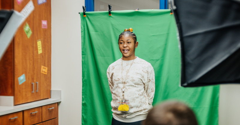 Charles England Elementary School student speaks in front of a green screen during a school video recording.