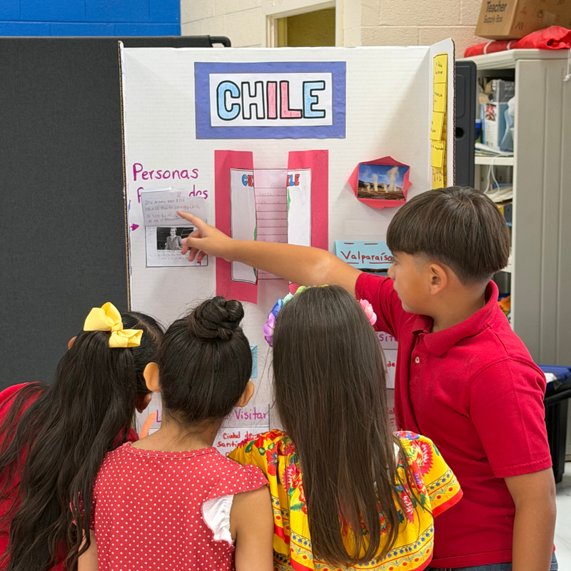 A Pickett Elementary School student presents a project about Chile to classmates gathered around a colorful informational display.