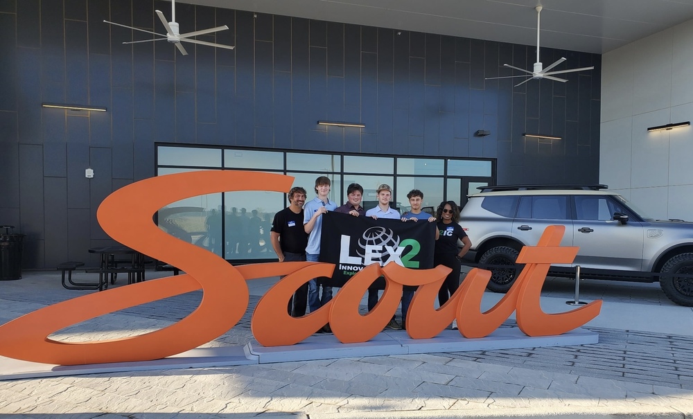 L2IC students and director Schiria Wilson pose in front of Scout Motors sign