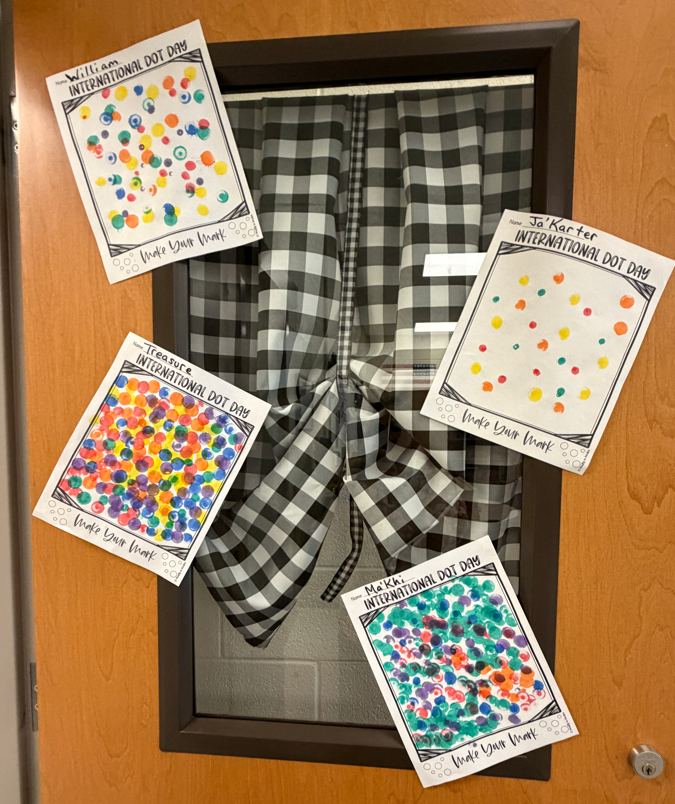 The outside of a classroom door is shown with four student work samples of their artwork showing how they used different colored dot stampers to make art.