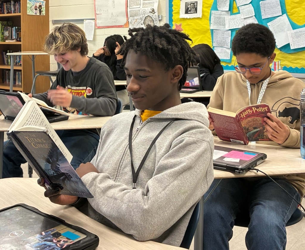 A male student reading  a book in his desk.
