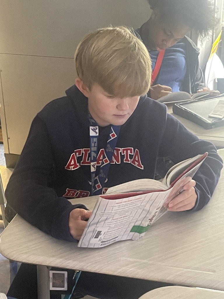 A male student reading  a book in his desk.