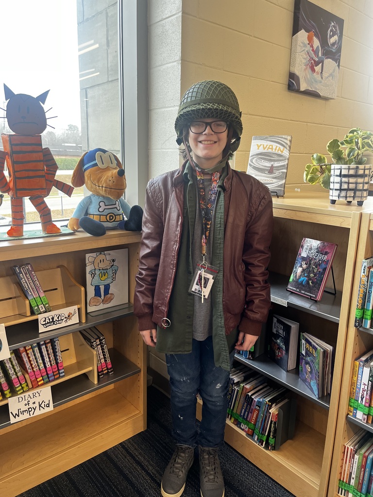 A male student smiling for the camera in the library dressed up as an explorer.