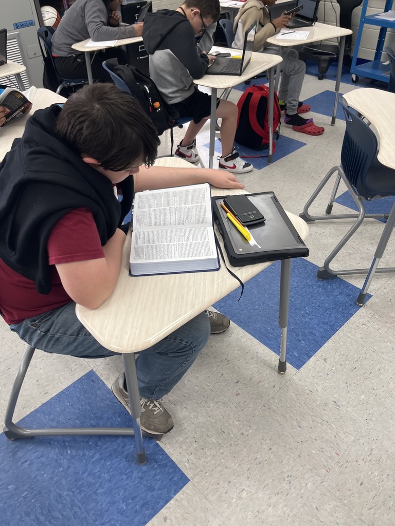 A male student reading  a book in his desk.