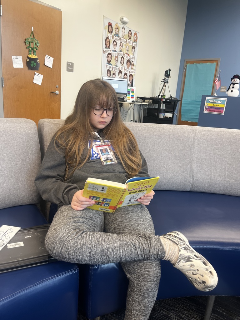 A female student sitting on a couch in the library reading a book.