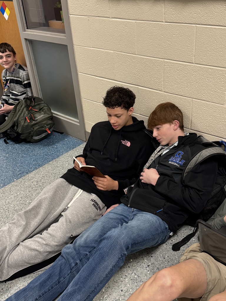 Two boys sitting on the floor in the hallway reading a book.