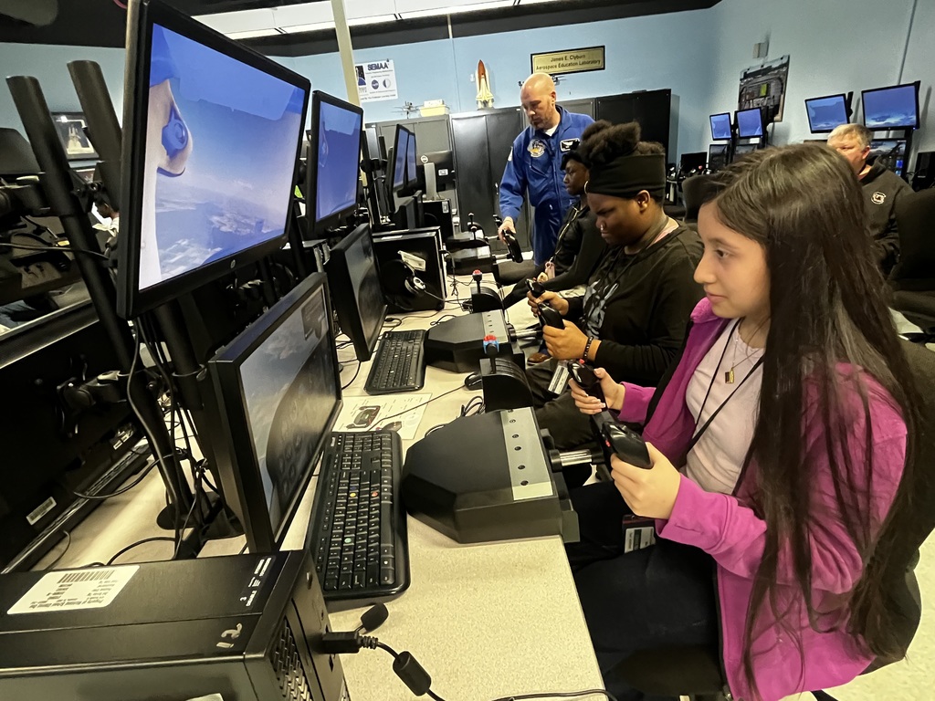 Students sit at a computer table and fly the flight simulators.
