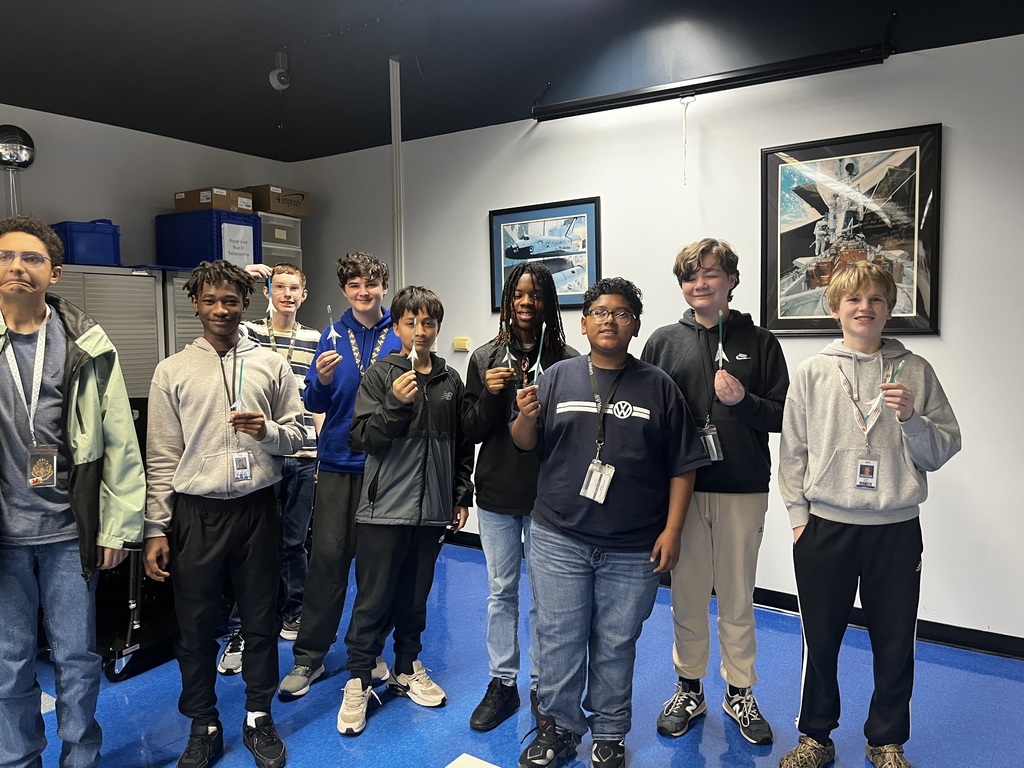 Boys smile for the camera while holding up their paper straw rockets they built before testing their distance.