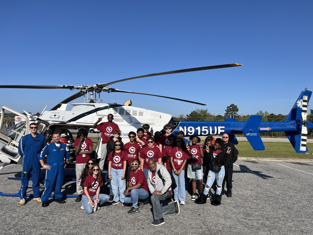 Group of students standing in front of helicopter smiling for the camera.